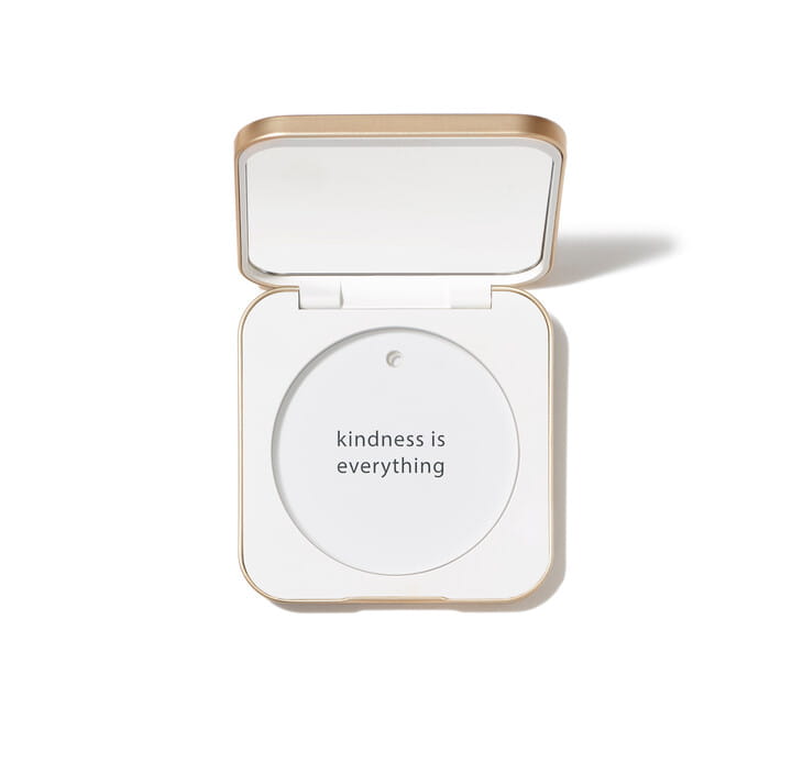 Na zdjęciu jest kompaktowe opakowanie wielokrotnego użytku marki jane iredale. Minimalistyczny, elegancki design w kolorze białym, napis na froncie: “you make the world more beautiful. Widać lusterko pod wieczkiem.