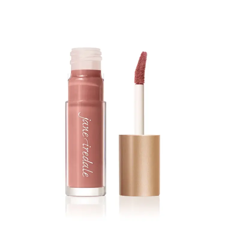Na zdjęciu przedstawiony jest błyszczyk do ust Jane Iredale w odcieniu Craving. Produkt zamknięty jest w eleganckim opakowaniu z przezroczystą tubką i złotą nakrętką. Odcień Craving to jasny, stonowany róż z nutą łososia