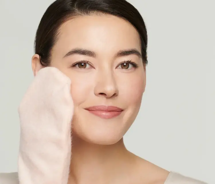 Na zdjęciu jest kobieta używającą rękawicy Magic Mitt marki Jane Iredale do oczyszczania twarzy. Kobieta wygląda na zrelaksowaną i zadowoloną, a jej cera jest promienna i świeża.