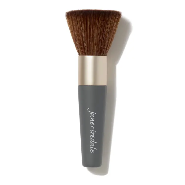 Na zdjęciu pędzel do makijażu marki Jane Iredale. Kształt główki: płaska, szeroka i gęsto zbita. Włosie: syntetyczne, miękkie, o brązowym kolorze. Trzonek: krótki, w kolorze szaro-grafitowym z logiem „jane iredale”