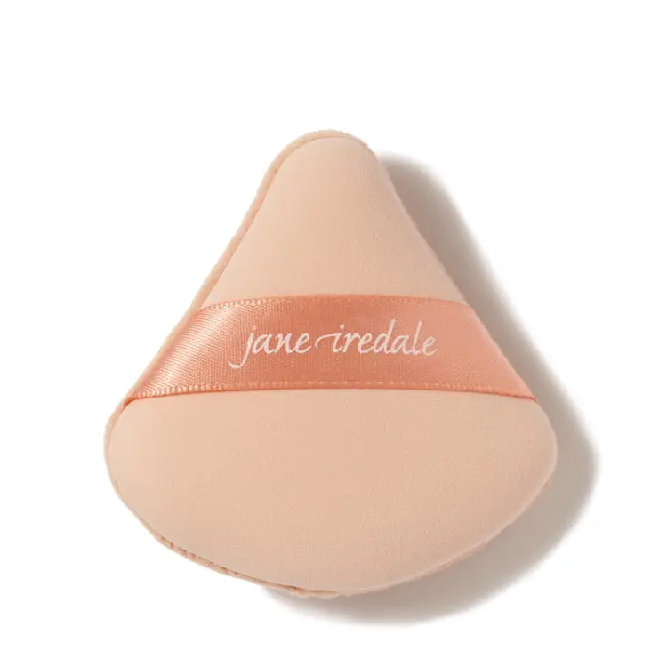 Na zdjęciu jest gąbka do makijażu marki jane iredale,  służąca do nakładania podkładu.  beżowy materiał,  trójkątny kształt – idealny do precyzyjnej aplikacji w okolicach oczu i nosa,  satynowa tasiemka z logo jane iredale ułatwiająca chwyt.