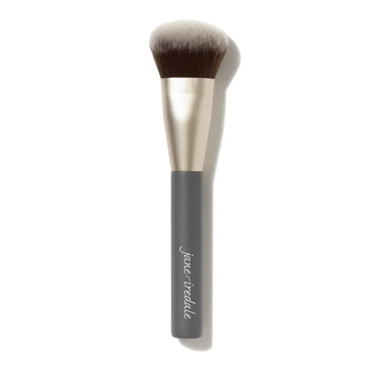Na zdjęciu jest pędzel do makijażu marki jane iredale. Ma lekko skośnie ścięte, gęste włosie w odcieniach brązu i bieli oraz ciemny trzonek z białym logo marki. To pędzel typu multi-use, do aplikacji produktów sypkich, prasowanych lub w kremie.