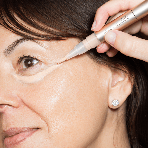 Na zdjęciu jest aplikacja korektora Jane Iredale Active Light. Produkt w formie pisaka z pędzelkiem nakładany jest pod oko. Skóra modelki w średnim wieku wygląda na zdrową i promienną.