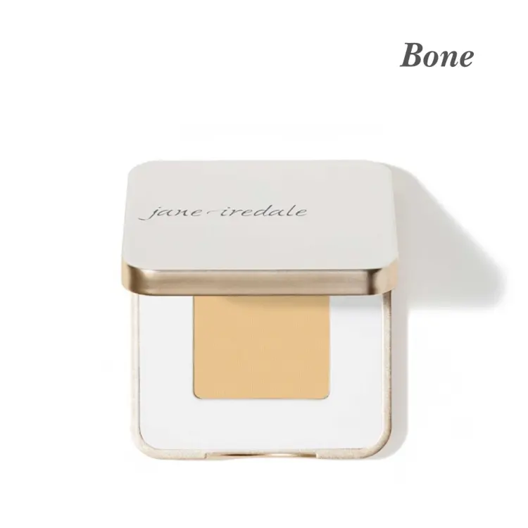 Cień do powiek Jane Iredale w odcieniu Bone. Produkt jest w eleganckim, białym etui ze złotym wykończeniem. Odcień Bone jest nieco cieplejszy i bardziej żółtawy niż French Vanilla, idealny dla skóry o jasnej karnacji z ciepłymi podtonami.