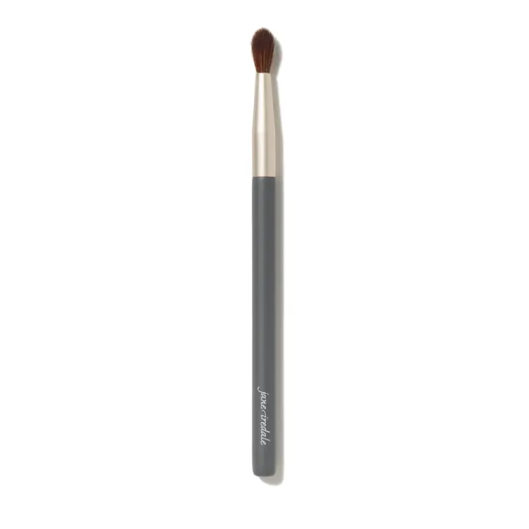 Na zdjęciu znajduje się pędzelek do oczu marki Jane Iredale. Ma elegancki, smukły trzonek w kolorze grafitu z napisem,  ściętą końcówkę z ciemnego włosia.  Pędzel jest przeznaczony do precyzyjnego nakładania cieni.
