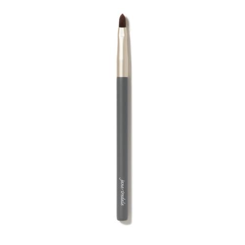 Na zdjęciu jest cienki pędzelek do makijażu jane iredale. Ma smukły kształt, szarą rączkę z logo marki i złotą skuwkę. Włosie pędzelka jest krótkie, ścięte w szpic, co sprawia, że idealnie nadaje się do precyzyjnej aplikacji produktów.