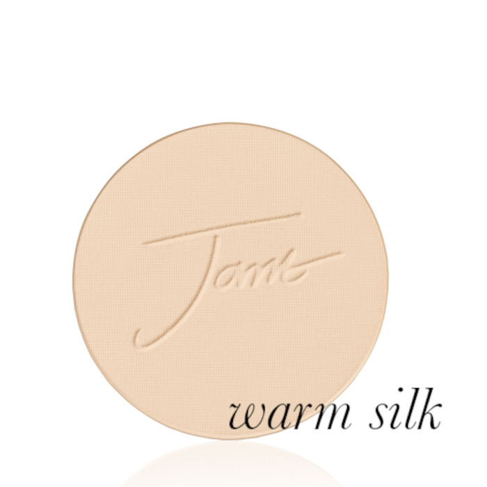 Okrągły, prasowany puder do twarzy marki Jane Iredale w odcieniu Warm Silk: jasny beż z ciepłym, złocistym podtonem z wytłoczonym logo Jane Iredale.