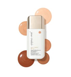 Na zdjęciu znajduje się produkt Jane Iredale Glow Fixation SPF 40 Sheer Tint Skin Enhancer w białym opakowaniu z aplikatorem. Wokół są próbki kosmetyku w odcieniach od jasnego beżowo-brzoskwiniowego do ciemniejszych, ciepłych brązów.