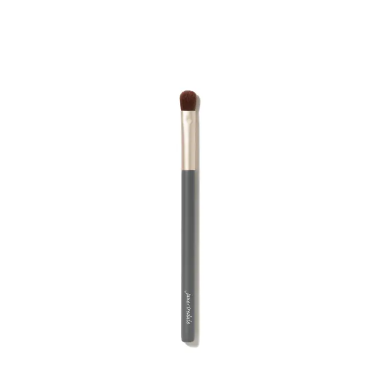 Zdjęcie przedstawia pędzelek do makijażu oczu jane iredale Flat Eye Brush na białym tle. Ma długi, szary trzonek z białym logo marki, złotą skuwkę oraz krótkie, gęste, płasko ułożone brązowe włosie o lekko zaokrąglonej końcówce.