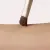 Zdjęcie przedstawia zbliżenie pędzelka jane iredale Flat Eye Brush podczas kontaktu ze skórą. Gęste, płasko ułożone brązowe włosie delikatnie dotyka przedramienia, ukazując kształt i precyzję końcówki. Widoczna jest również złota skuwka pędzelka.