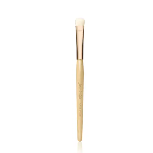 Na zdjęciu widoczny jest pędzel do makijażu marki Jane Iredale. Jest to cienki, precyzyjny pędzel o długim, drewnianym trzonku w naturalnym kolorze, z elegancką, złotą skuwką. Główka pędzla jest mała, zaokrąglona, wykonana z jasnego włosia.