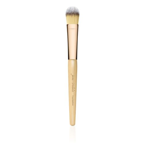 Na zdjęciu znajduje się pędzel do makijażu marki Jane Iredale. Ma elegancki design – drewniany trzonek w naturalnym kolorze z złotą skuwką i gęste, miękkie włosie w odcieniach żółci i bieli.